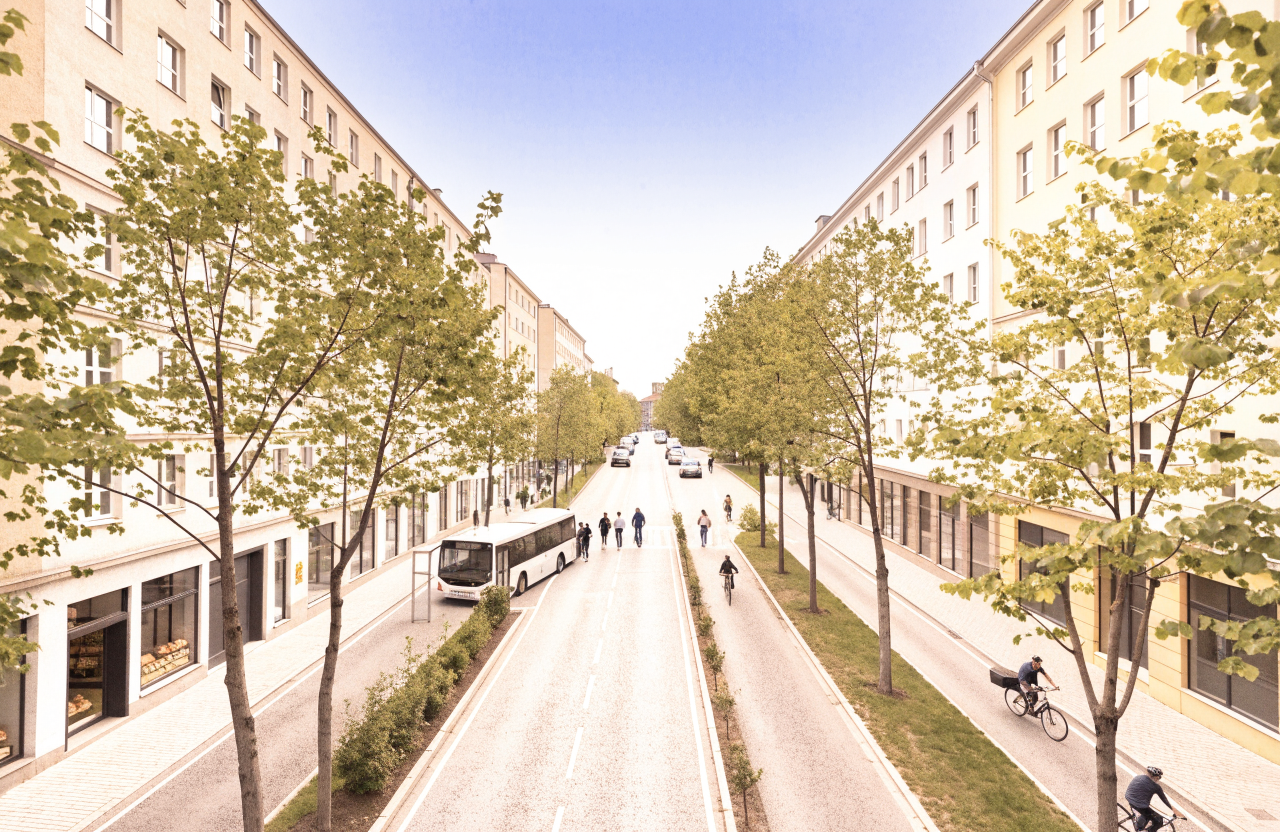 Seen from an upper window, a city crossroads where a bus has stopped beside a shelter and people cycle along a wide track. The outer lanes that once carried cars are now a bus lane and a cycle track, with only a few cars left waiting at the lights.