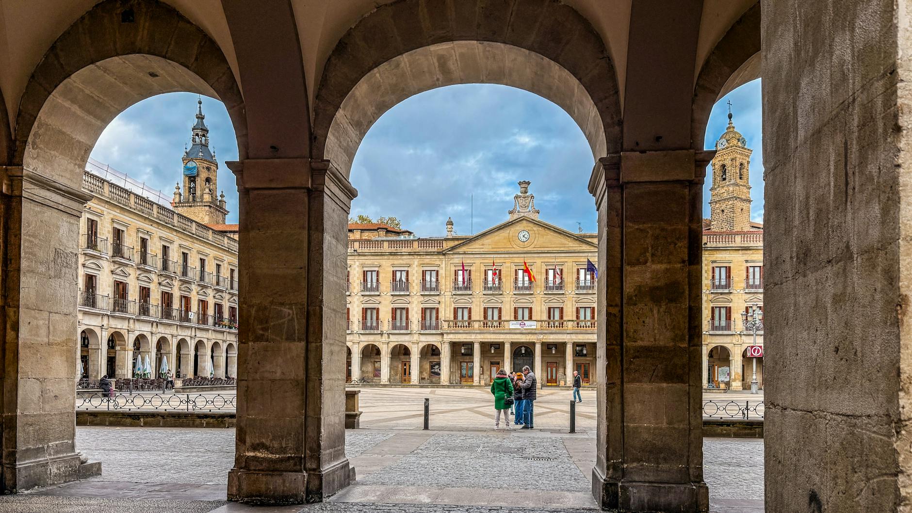 View of a historic Spanish square through an archway, featuring old architecture.
